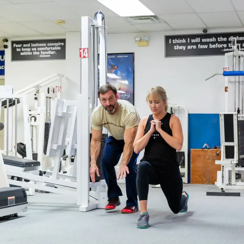 Tim crouched beside a client checking her lunge form